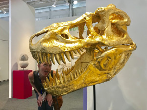 Alisha peeking out from the teeth of a gold plated dinosaur skull