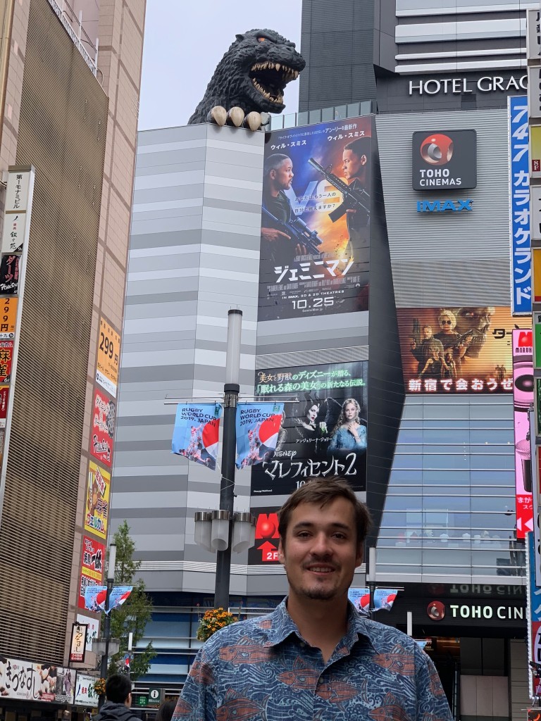2019, John in Tokyo with Godzilla  looming over the top of a downtown Tokyo skyscraper.